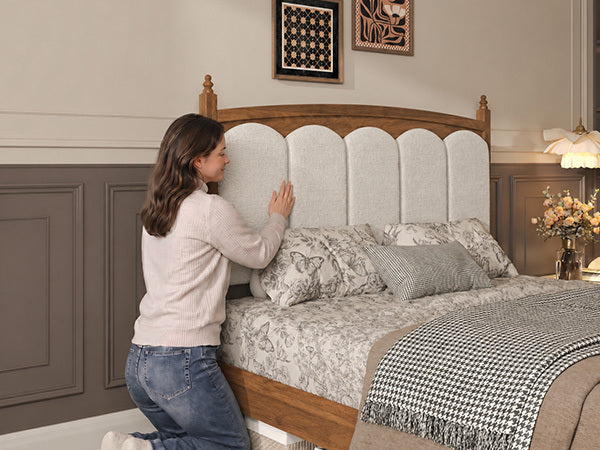 Person leaning on the cream padded headboard of the brown wood vintage queen bed