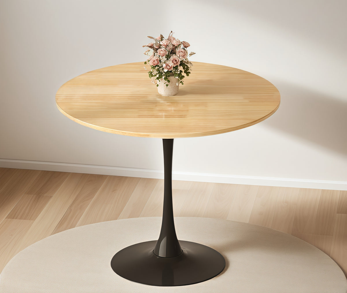 Front view of the natural wood round bistro table with pink flowers on a round rug near a white wall