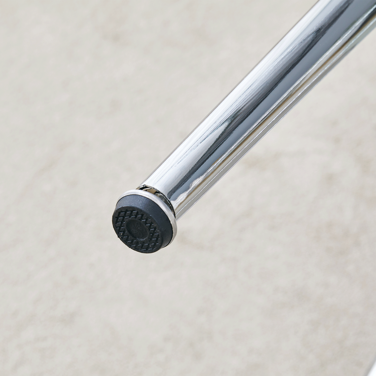 Close-up of a chrome leg foot with a black non-slip pad resting on carpet